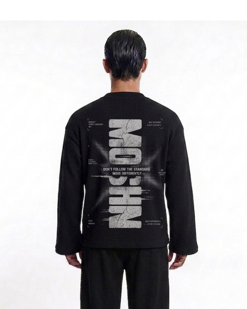A man viewed from behind wearing a black long-sleeve knit sweater with a large white graphic print on the back. The print features the word 'MOSCHINO' vertically in a distressed stencil font with technical drawing elements and the text 'DON'T FOLLOW THE STANDARDS' and 'HOW DIFFERENTLY?' around it.