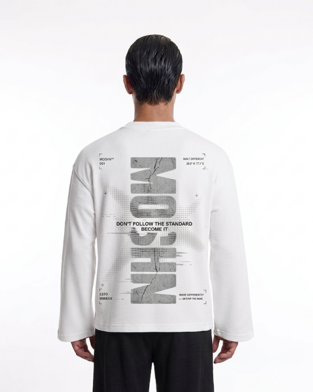 A model viewed from the back wearing a white long-sleeve t-shirt with a large gray graphic print on the back, paired with black pants, against a plain white studio background.