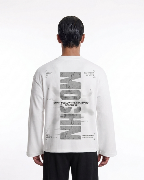 A model viewed from the back wearing a white long-sleeve t-shirt with a large gray graphic print on the back, paired with black pants, against a plain white studio background.